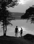 Man And Woman In Bathing Suits Holding Hands Watching Sunset Lakeside