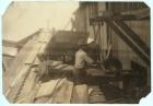 Charlie McBride aged 12 takes wood from a chute for 10 hours at Miller & Vidor Lumber Company, Beaumont, Texas for which he earns 50 cents while the other boy saws it on an unguarded circular saw, 1913 (b/w photo)