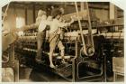 Small boys climbing on spinning frame to mend broken threads and replace empty bobbins at Bibb Mill, Macon, Georgia, 1909 (b/w photo)