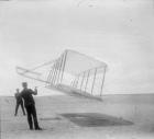 Wilbur Wright at left and Orville Wright at right, with a glider flying as a kite near the ground, 1901