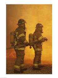 Rear view of two firefighters extinguishing a fire | Obraz na stenu