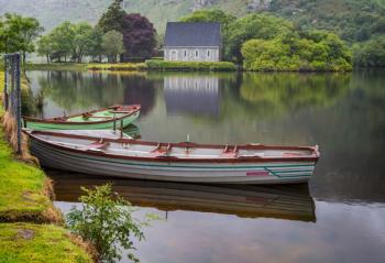 Gougane Barra, County Cork, Republic of Ireland. Eire. Looking across rowing boats moored at the lake shore with the Hermitage of St. Finbarr in the background. (photo) | Obraz na stenu
