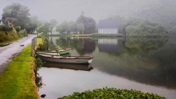 Gougane Barra, County Cork, Republic of Ireland. Eire. Looking across rowing boats moored at the lake shore with the Hermitage of St. Finbarr in the mist in the background. (photo) | Obraz na stenu